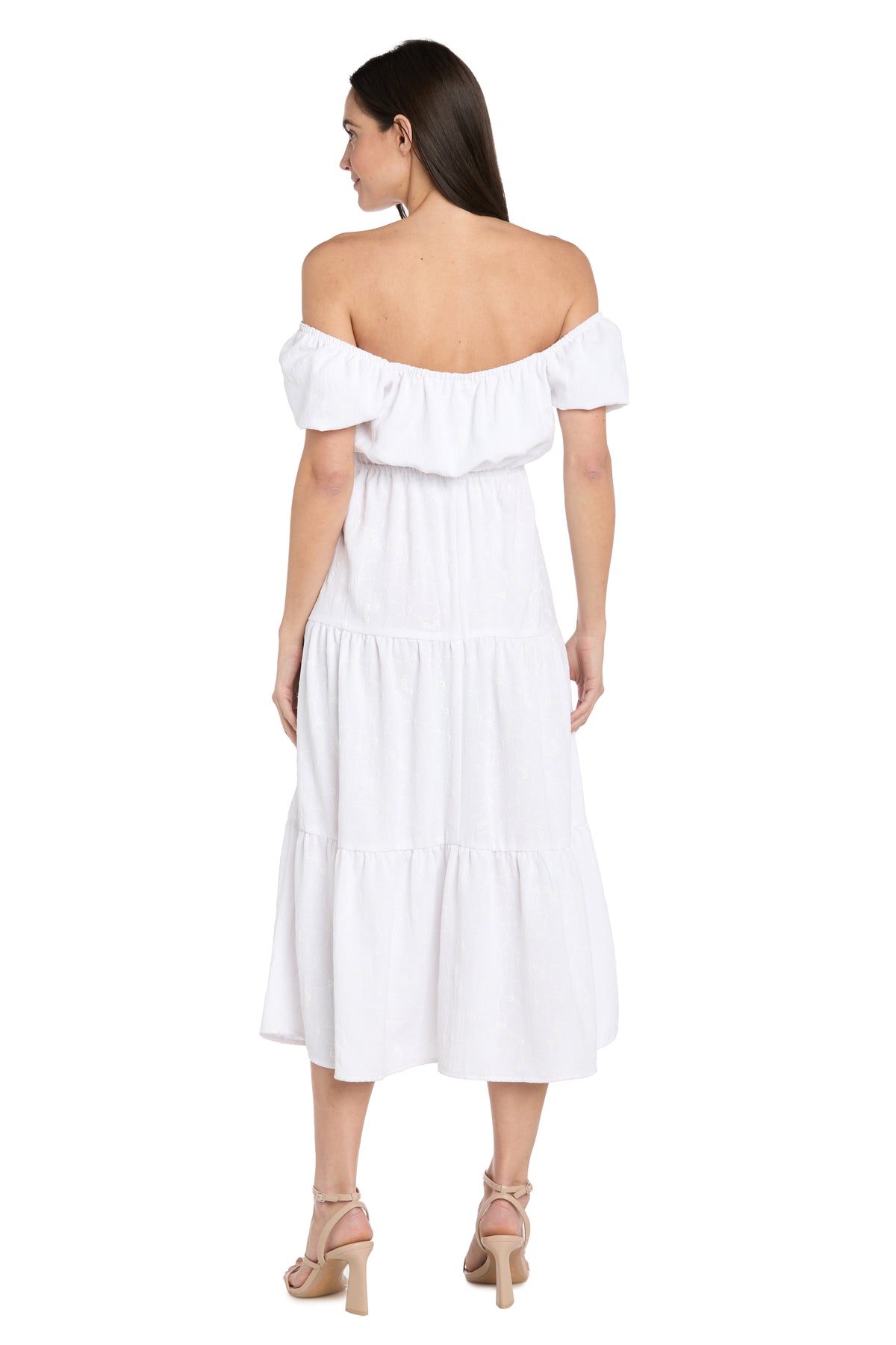 Woman stands with her back to the camera, wearing the R&M Richards 6669 Tea-Length White Party Dress featuring ruffled off-the-shoulder sleeves and a midi hem—ideal for special occasions. She's styled with beige heeled sandals.